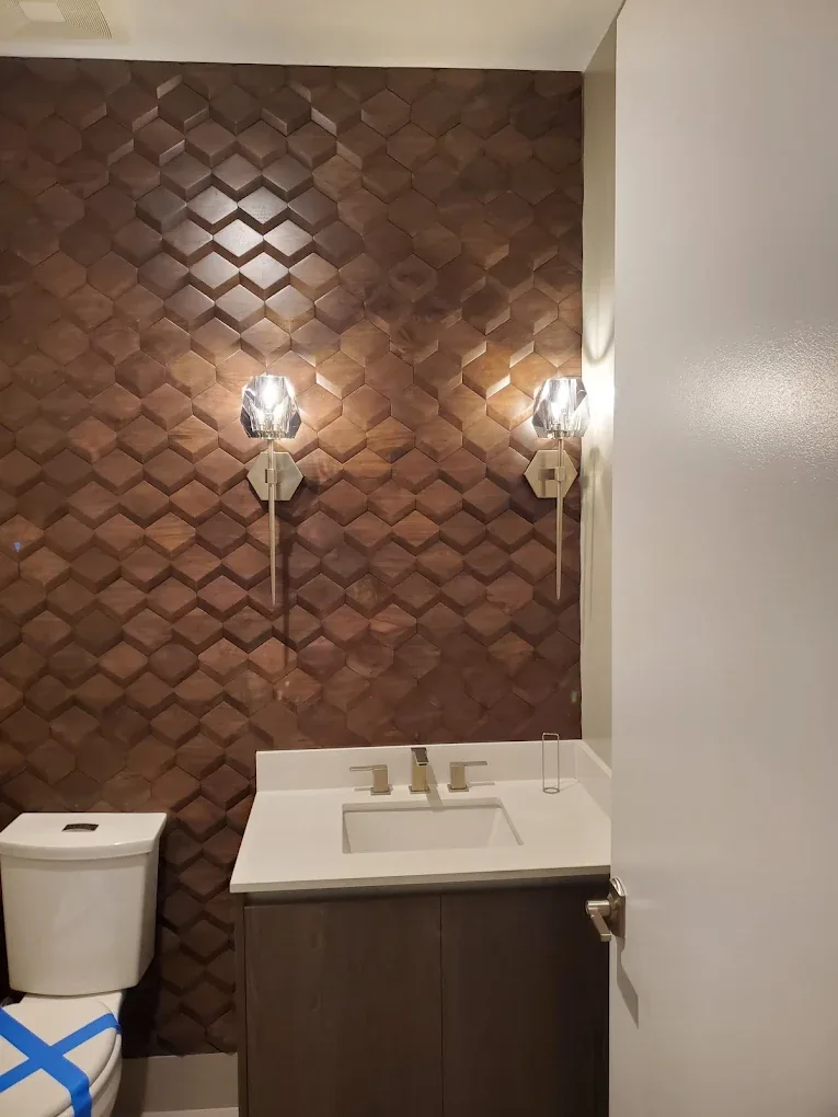 Two crystal sconces mounted on a geometric wood feature wall in a powder room